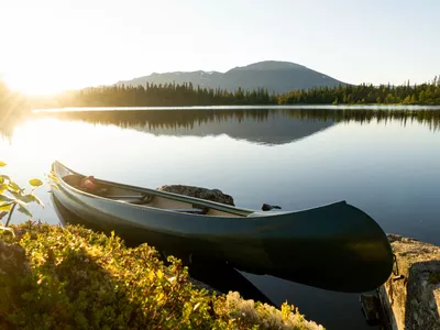 Grønn kano, i bakgrunnen er det skog, fjell og solnedgang.