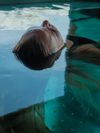 Jente som ligger med hodet opp i poolen.