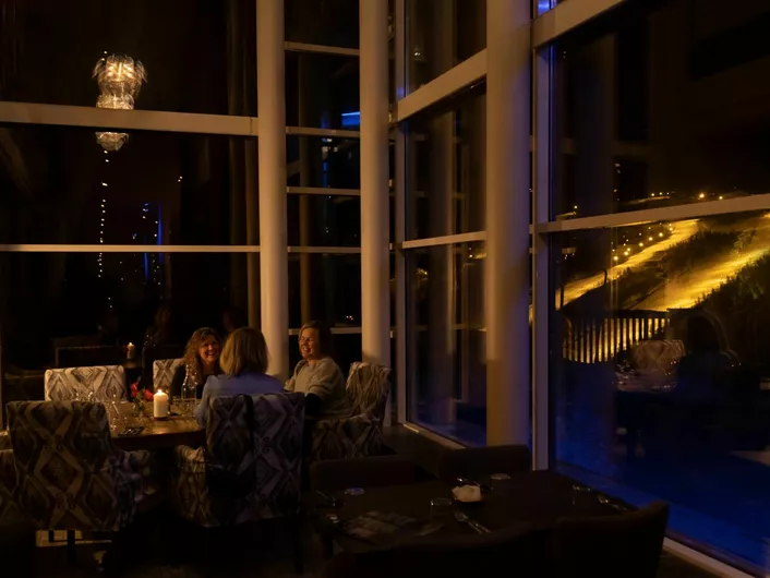 Tre damer som hygger seg på skarsnuten, i bakgrunnen er det skibakken på kveldstid.