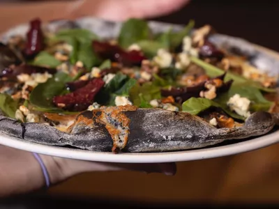 To hender som holder en svart pizza med delikat topping.