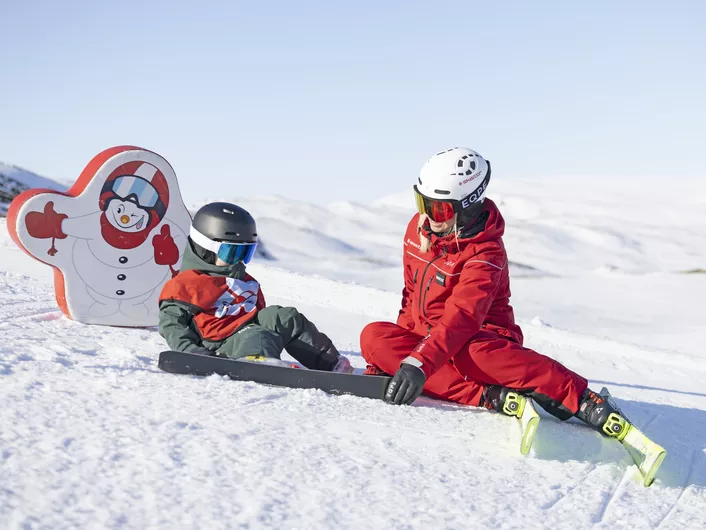 Skilærer og elev i skiskolen sitter i bakken