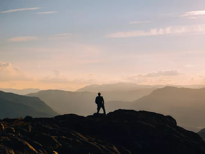 Person på toppen av et fjell i morgen disen.